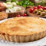 Chicken pie with cottage cheese, tomatoes, onion and olives on w Chicken pie with cottage cheese, tomatoes, onion and olives on wooden table and white plate.